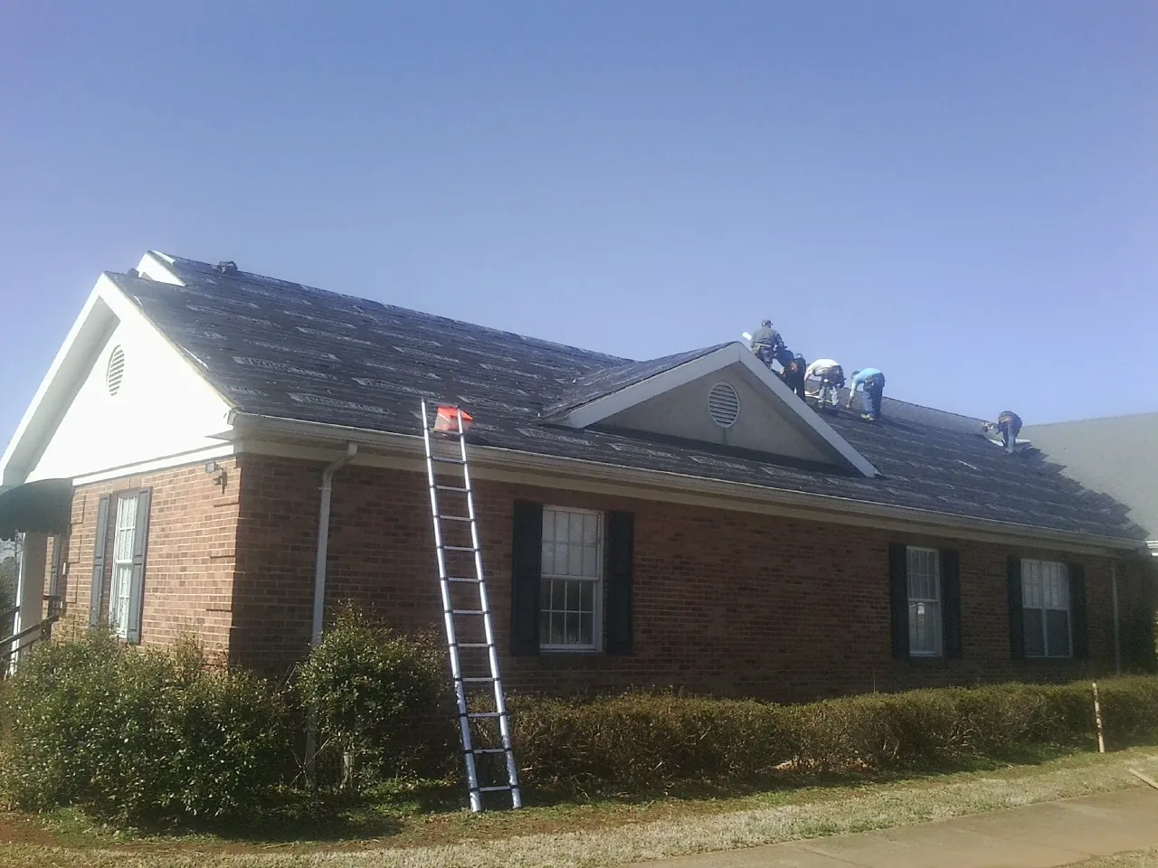 Crew tearing shingles off a brick ranch roof with a ladder set — Metal Roof Repair work by our crew in Oakdale
